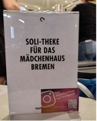 Auf dem Foto ist ein Aufsteller zu sehen, mit der Aufschrift "Soli-Theke für das Mädchenhaus Bremen"